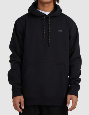 A person wearing a Billabong Shoreline Pullover—a casual black hoodie with a front pocket, black and white drawstrings, and a small rectangular chest patch—stands against a light gray background.