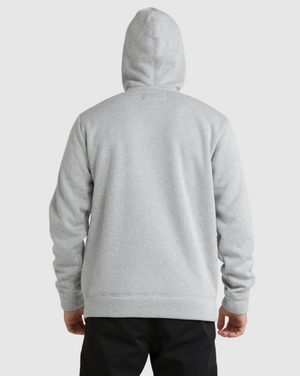 A person wearing a light gray Billabong Boundary Sherpa Zip hoodie, featuring cozy sherpa lining for added comfort, stands facing away from the camera with arms relaxed at their sides against a plain, light background.