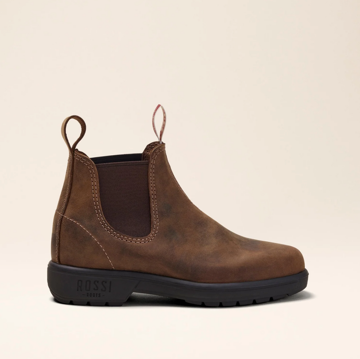 The Rossi Endura 303 Elastic Sided Boot is a brown Chelsea boot made from full grain leather. It features elastic side panels, front and back pull tabs, a slip-resistant black rubber sole with "ROSSI" embossed on the heel. The background is neutral beige.