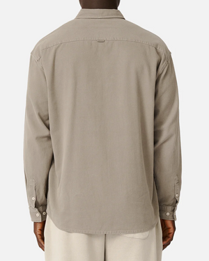 A person is shown from behind wearing the Industrie The Taylor Shirt in light taupe—a 100% cotton, long-sleeve button-up with a collar and buttoned cuffs. The shirt is worn untucked and paired with light-colored pants for a casual look.