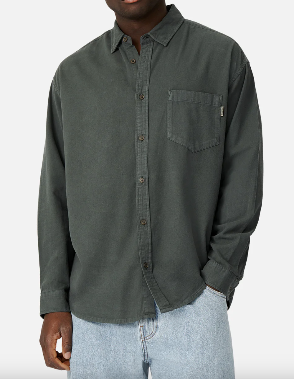 Wearing a dark green Industrie The Taylor Shirt with an Industrie logo and chest pocket, paired with light blue jeans. Made from 100% cotton for a comfortable fit, the shirt's sleeves are rolled down against a plain white background.