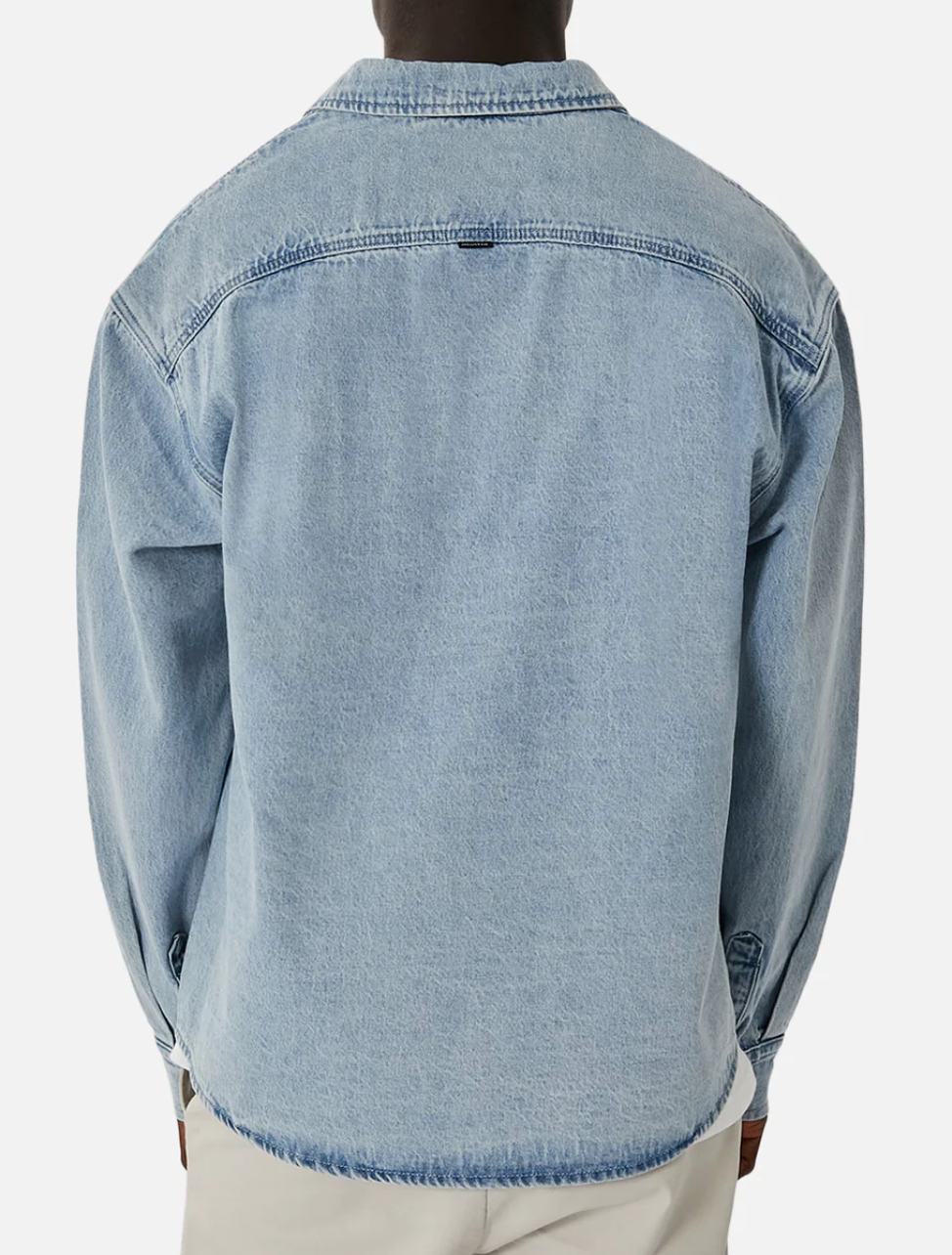 Wearing the Industrie The Lafayette Shirt, a light blue denim button-up with classic collar and long sleeves in 100% cotton, a person stands out against a plain white background. Paired with light-colored pants, the relaxed fit of this stylish piece is captured from behind.