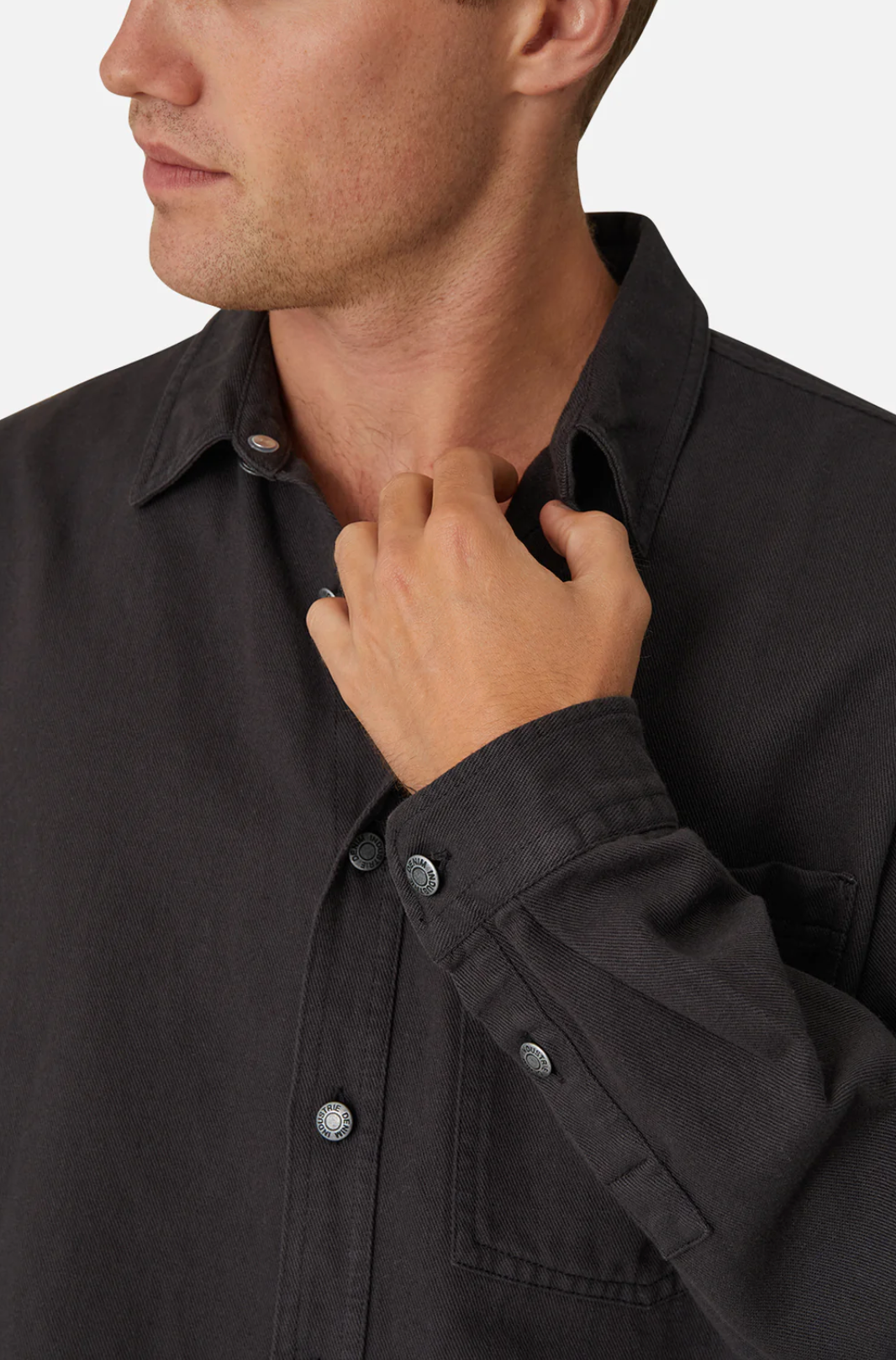 A person wears Industrie The Portland Shirt, a dark gray cotton/linen blend button-up, with the collar slightly turned up. They're touching the collar with their right hand, visible from torso to partial face against a white background.