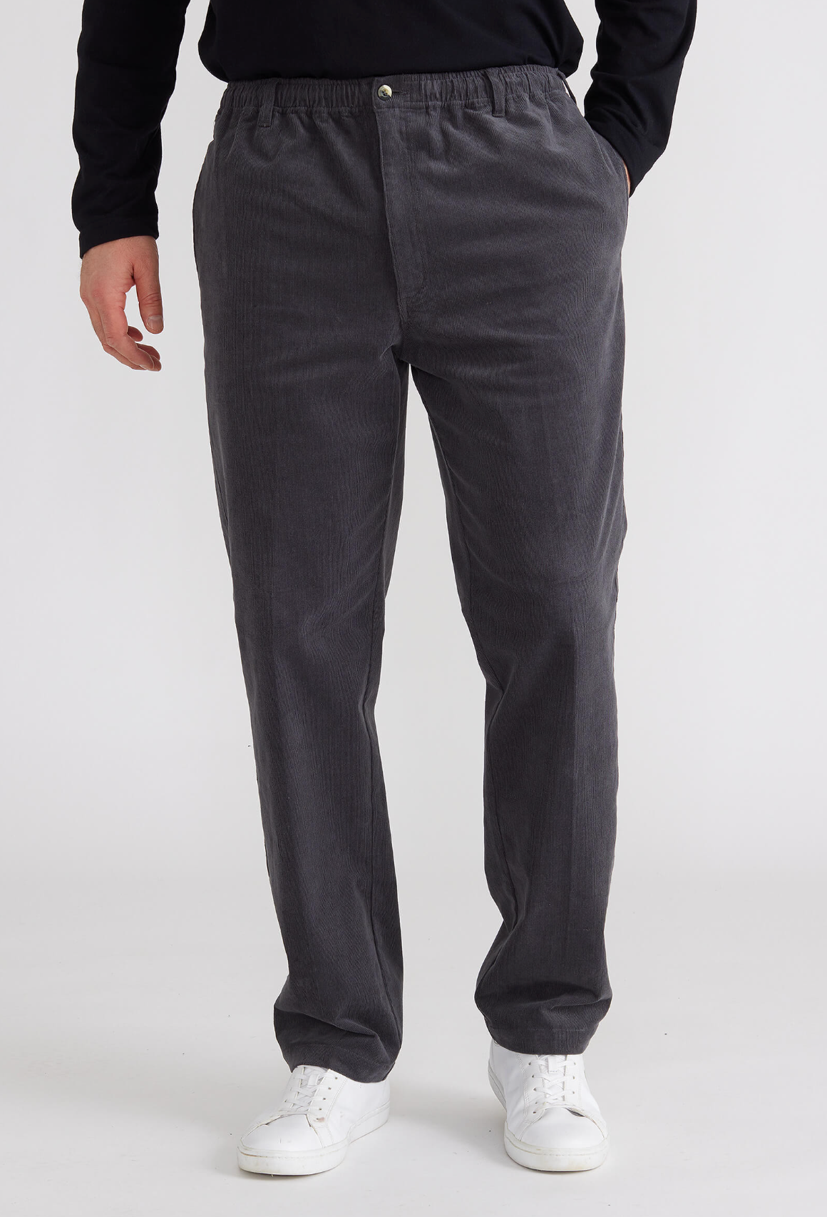 A person dons charcoal gray Breakaway Cordeaux Pants with an elastic waist, paired with white sneakers and a partially visible black top, against a plain backdrop.