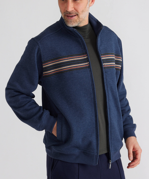 Wearing the Breakaway Bello Snowy Mt Fleece Jacket, featuring blue color and horizontal colorful stripes, paired with a black shirt and dark pants, they exude a casual vibe. With one hand in pocket, they're smiling and looking to the side.