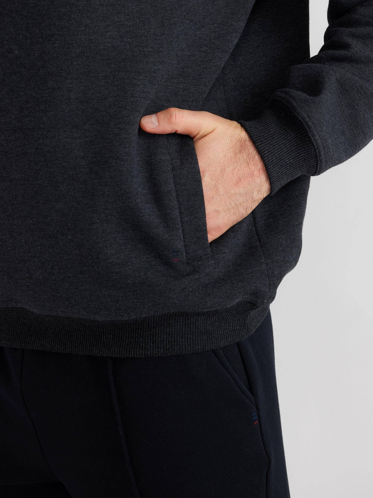 A person in a Breakaway Bello Snowy Mt Fleece Half Zip in dark gray and black pants casually rests their right hand in the front pocket. The plain white background adds to the relaxed and breakaway vibe.