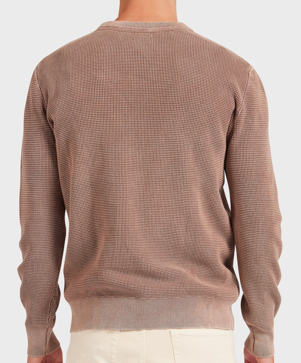 Wearing the Academy Brand Newport Crew Knit, a 100% cotton, long-sleeve beige sweater with subtle patterns and ribbed hem and cuffs, the person pairs it with light-colored pants. They're photographed from the back against a plain background.