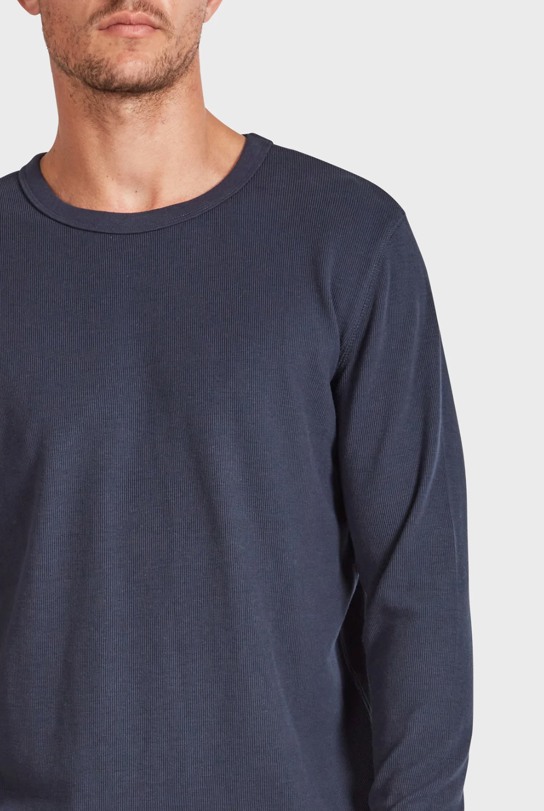 A person wearing an Academy Brand Workers Crew, a long-sleeved dark blue ribbed shirt with a crew neck, is partially visible against a plain white background, with their face not fully shown.