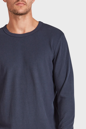 A person wearing an Academy Brand Workers Crew, a long-sleeved dark blue ribbed shirt with a crew neck, is partially visible against a plain white background, with their face not fully shown.
