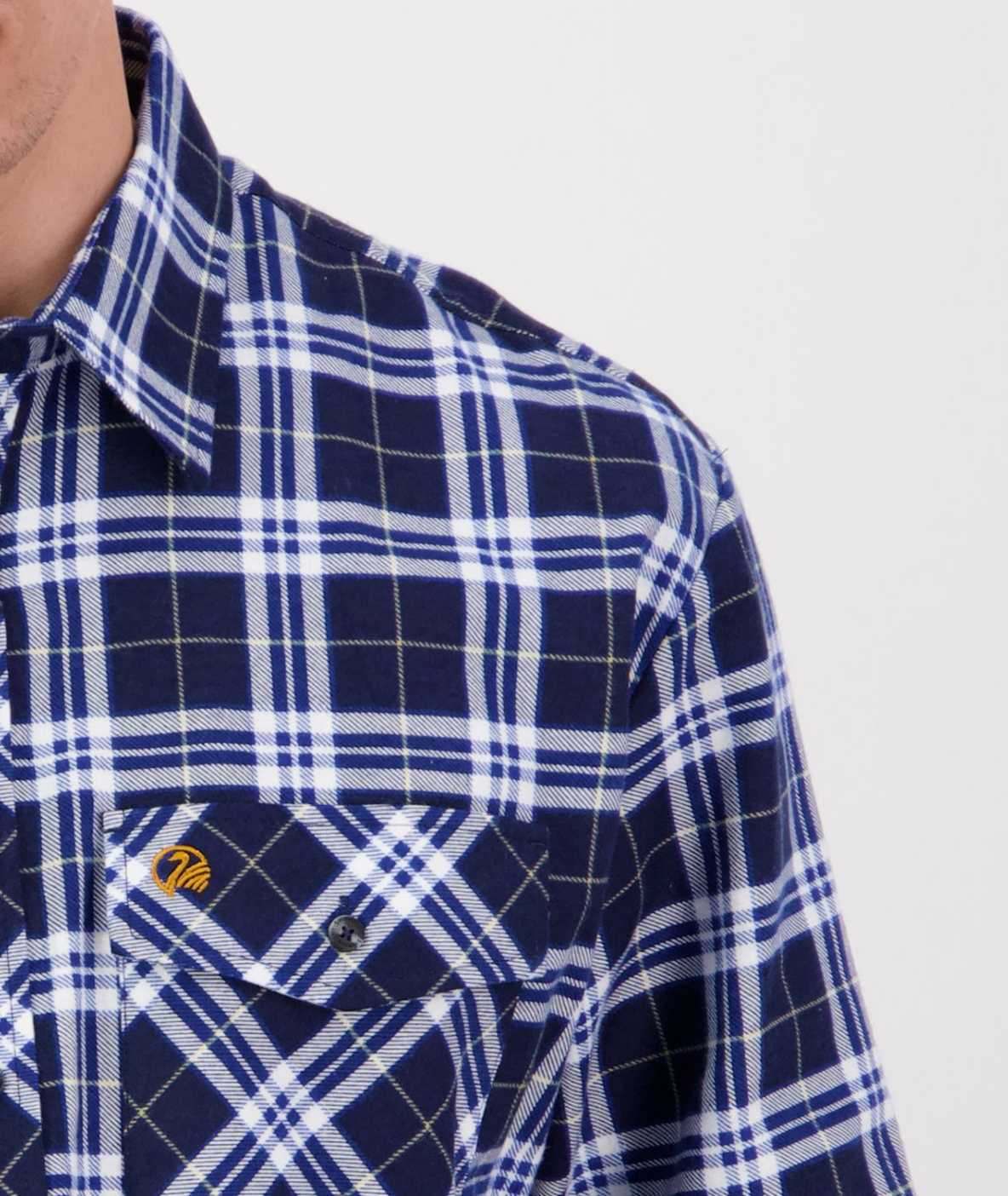 Close-up of an individual wearing a Swanndri Egmont Flannelette shirt with blue and white plaid, made from brushed cotton. This long sleeve features a buttoned pocket with a logo above it, set against a plain white background.