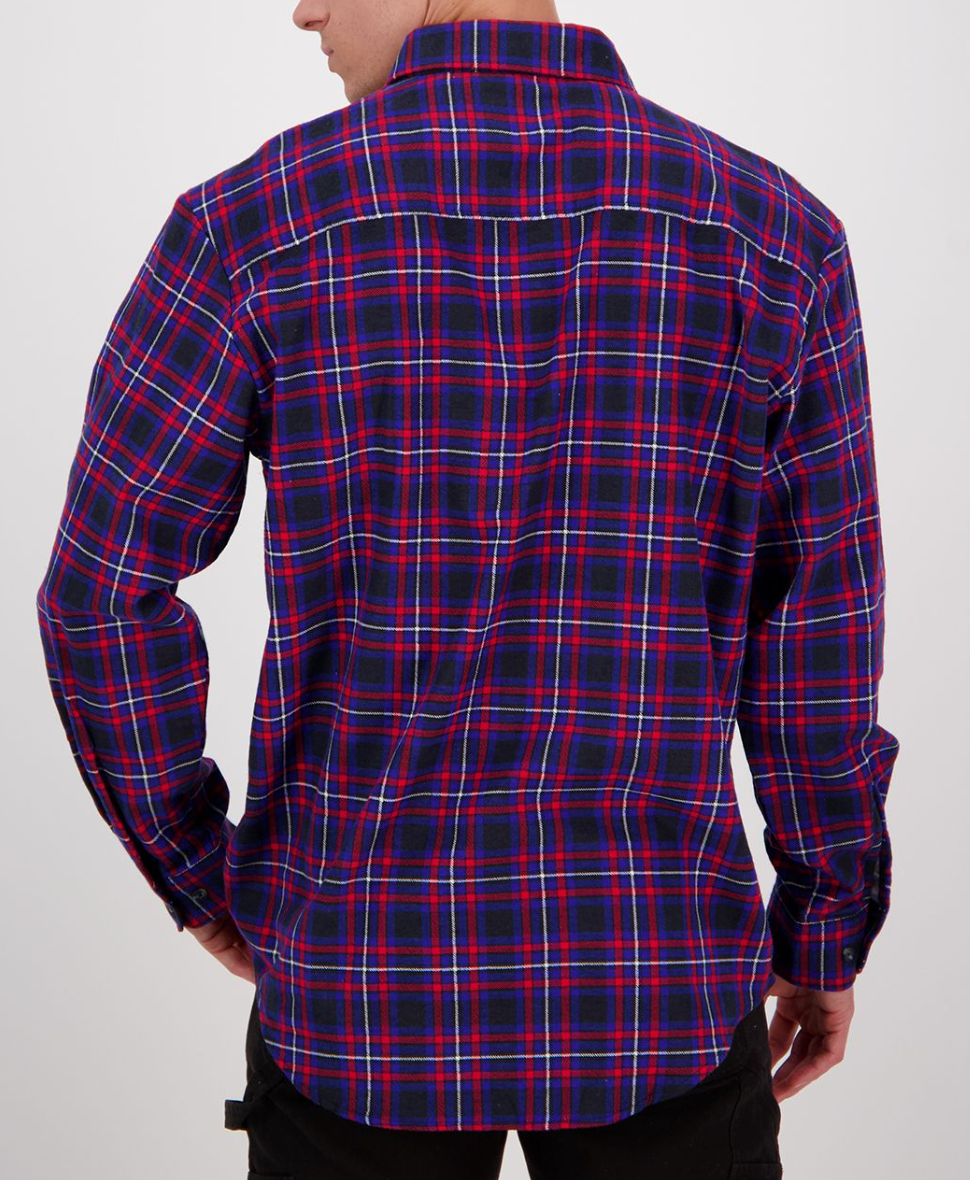 The individual is wearing a vibrant plaid shirt in red, blue, and black from the Swanndri Egmont Flannelette Twin Pack. Seen from behind, it boasts long sleeves with buttoned cuffs and a collar. Their left hand rests casually on their hip.