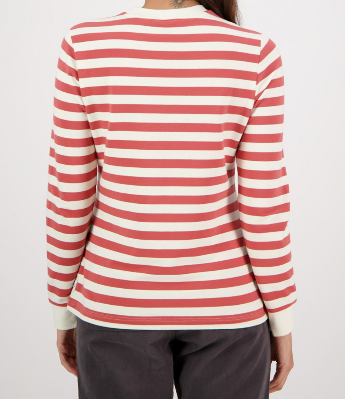 Wearing a Swanndri Papamoa Stripe Long Sleeve Tee with bold red and white horizontal stripes, paired with black pants, the individual stands against a plain white backdrop facing away.