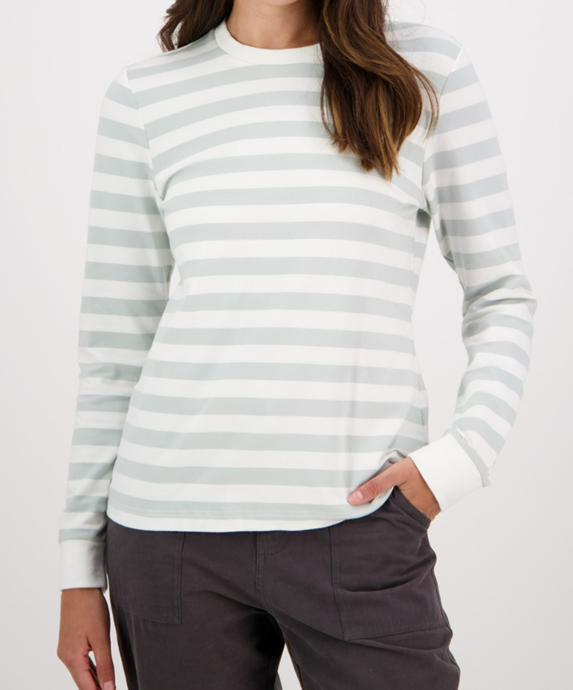 Someone models the Swanndri Papamoa Stripe Long Sleeve Tee with light gray and white stripes, casually slipping a hand into the pocket of dark gray pants against a plain white background.