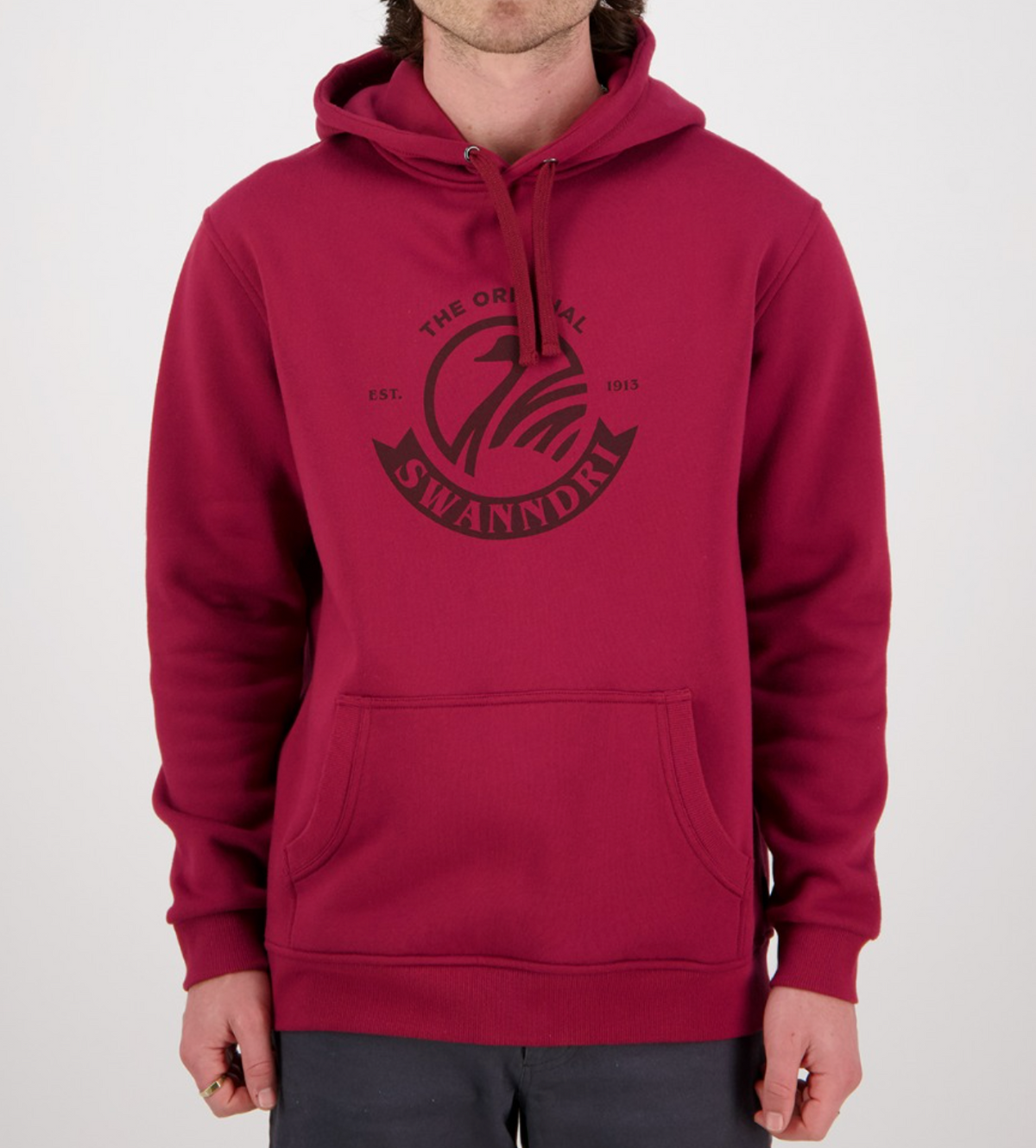 A person in a casual red Swanndri Original Fleece Hoody with a kangaroo pocket and drawstring hood poses against a plain white background, featuring "The Original SwannDri Est. 1913" in a circular logo on the chest.