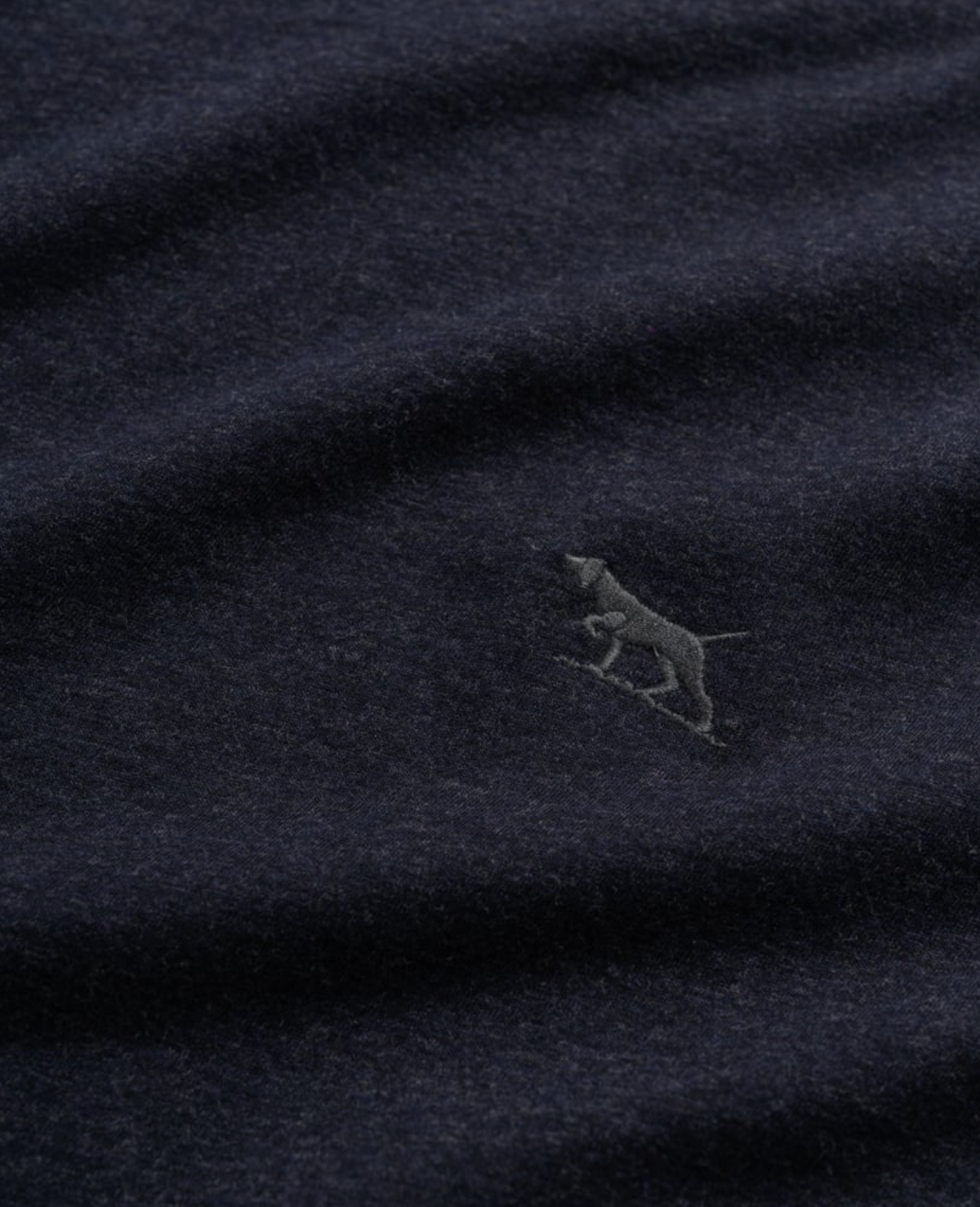 The Rodd & Gunn Long Sleeve Gunn T-Shirt is a dark blue, 100% cotton fabric with a subtle texture in a sports fit. It features an embroidered silhouette of a small dog, standing and facing left, on the lower right side.
