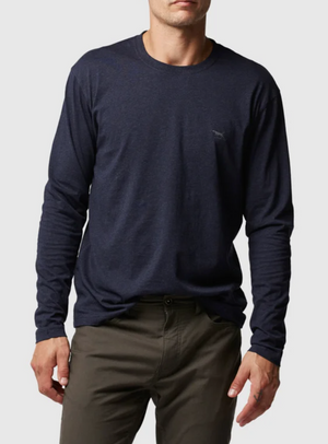 A person stands against a plain backdrop wearing a dark blue Rodd & Gunn Long Sleeve Gunn T-Shirt, featuring a sports fit and small chest logo, paired with olive green pants. Their face is unseen.