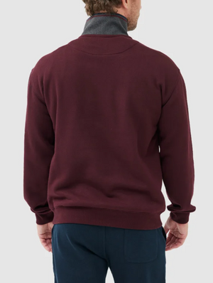 The individual, wearing the Rodd & Gunn Alford Forest Sweat—a maroon sweatshirt with a gray collar and half zip front—faces away to display its back. They pair it with dark pants against a plain light gray backdrop.