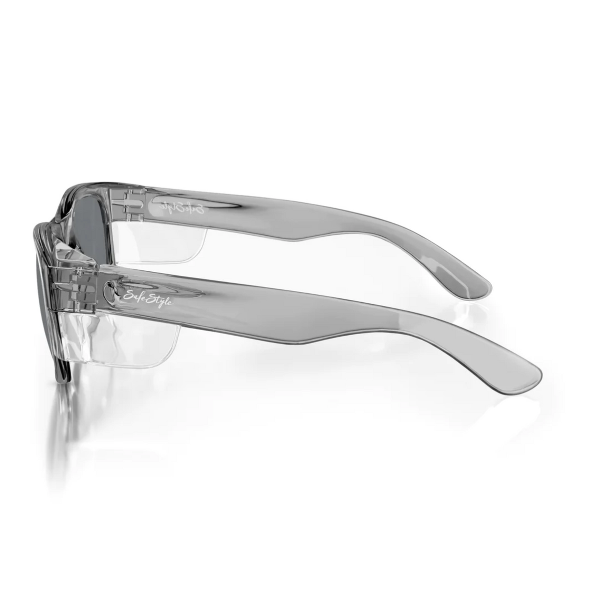 SafeStyle Classics safety glasses with clear rims, tinted lenses, and wide grey temples feature a graphite frame for UV protection. An engraved logo adorns the temples, all presented on a reflective white surface from a side angle.