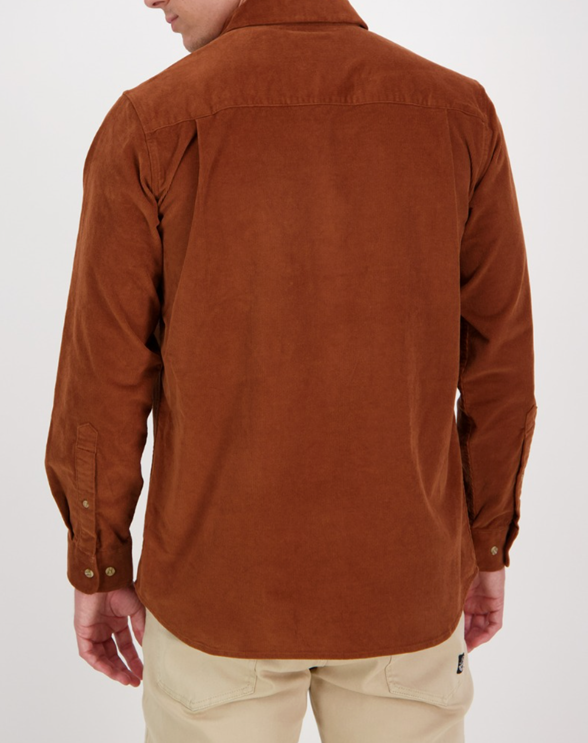 A person is shown from behind wearing a Swanndri Ranfurly Corduroy Shirt, featuring buttoned cuffs, paired with beige pants against a white background.