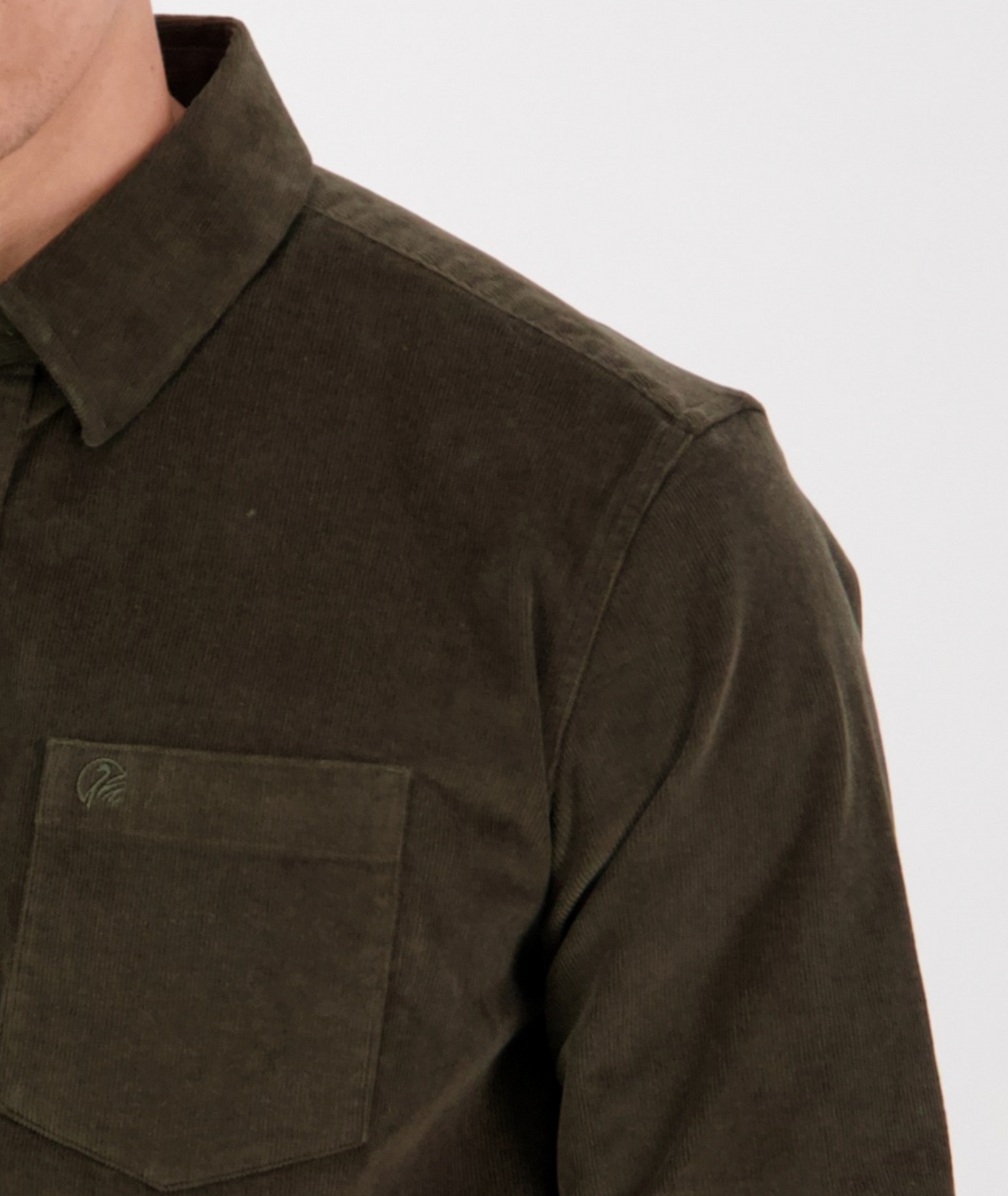 A close-up shows a person wearing the tailored Swanndri Ranfurly Corduroy Shirt in dark green with a left front pocket. It's buttoned up, and the heavy cotton fabric looks soft and textured against a neutral background.