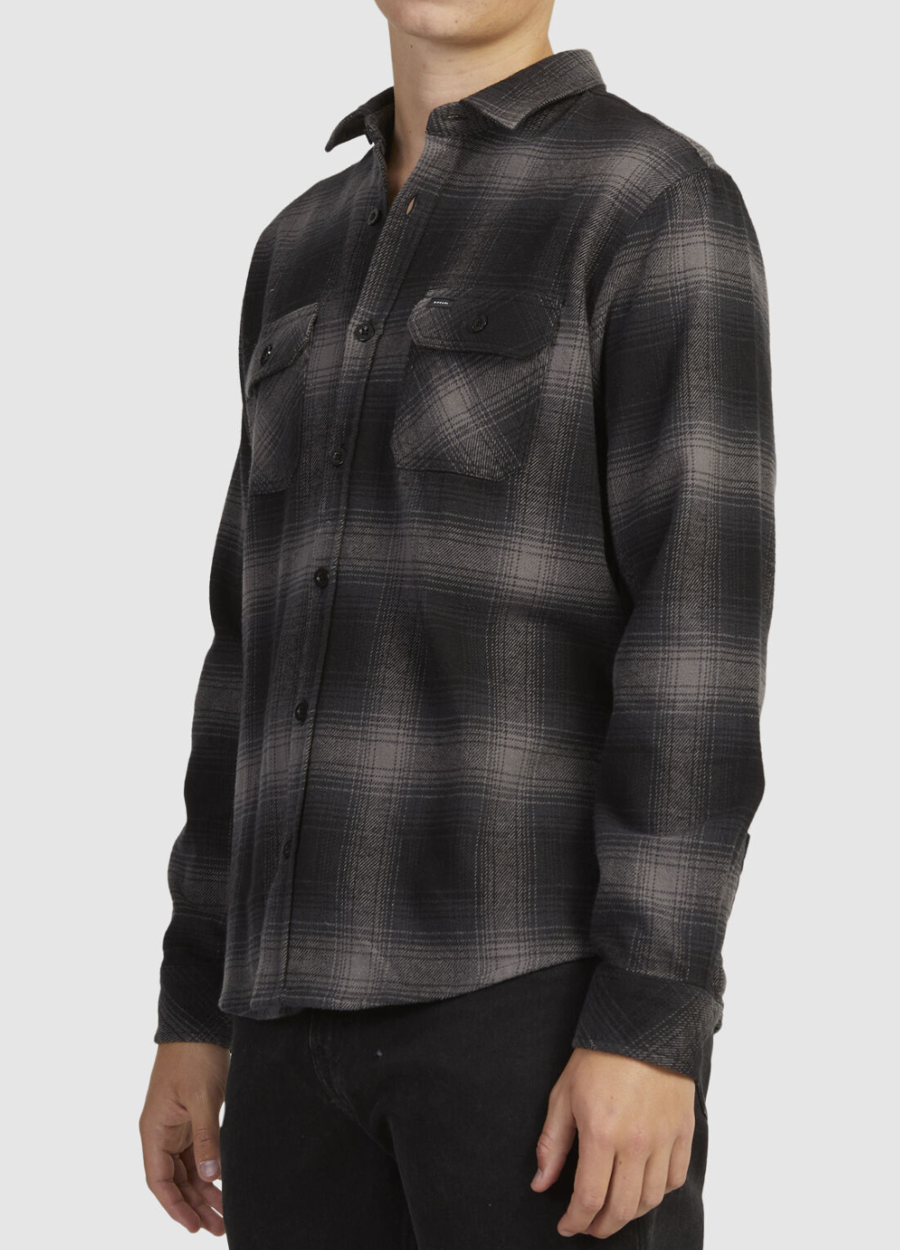 A person is wearing the Rip Curl Count Flannel Shirt, made from brushed cotton in a black and gray plaid with two chest pockets, paired seamlessly with black pants. The face is out of frame, highlighting the chic ensemble.