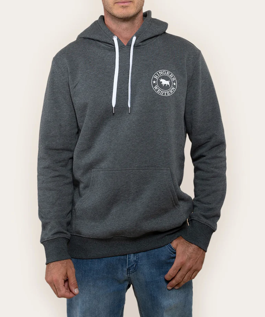 A person in a dark gray Ringers Western Signature Bull Hoodie with white drawstring and circular logo on the chest pairs it with blue jeans against a neutral background.