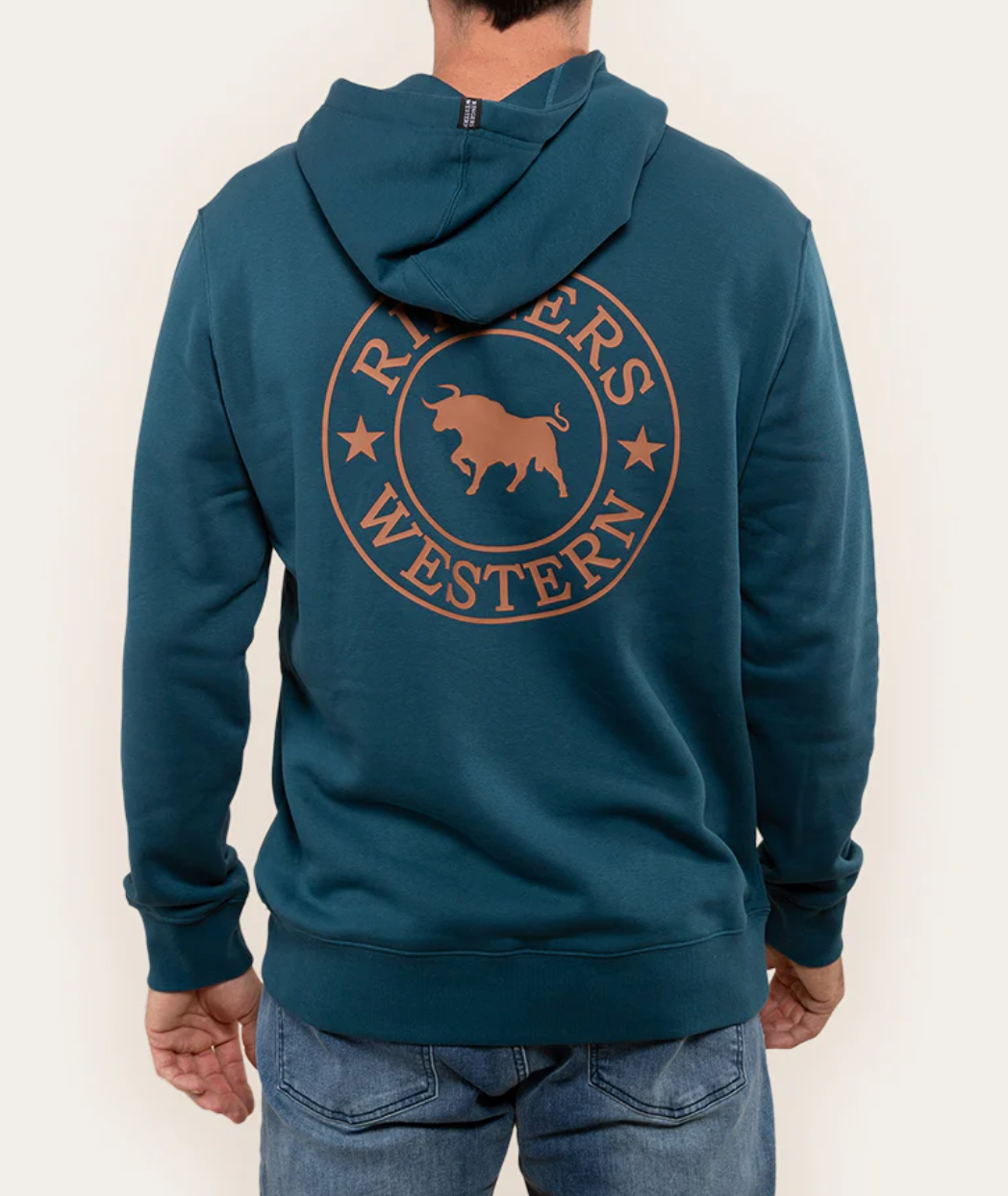 A person in a Ringers Western Signature Bull Hoodie with a circular logo and teal cotton fabric stands facing away, hands at their sides, paired with blue jeans.