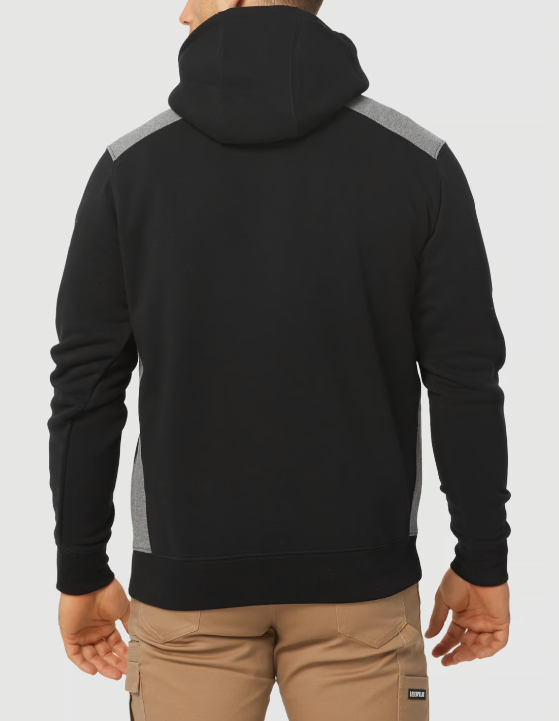 A person in khaki pants is seen from the back wearing a black CAT Logo Panel Hooded Sweat with gray shoulder accents, featuring a large front pocket and no visible designs.