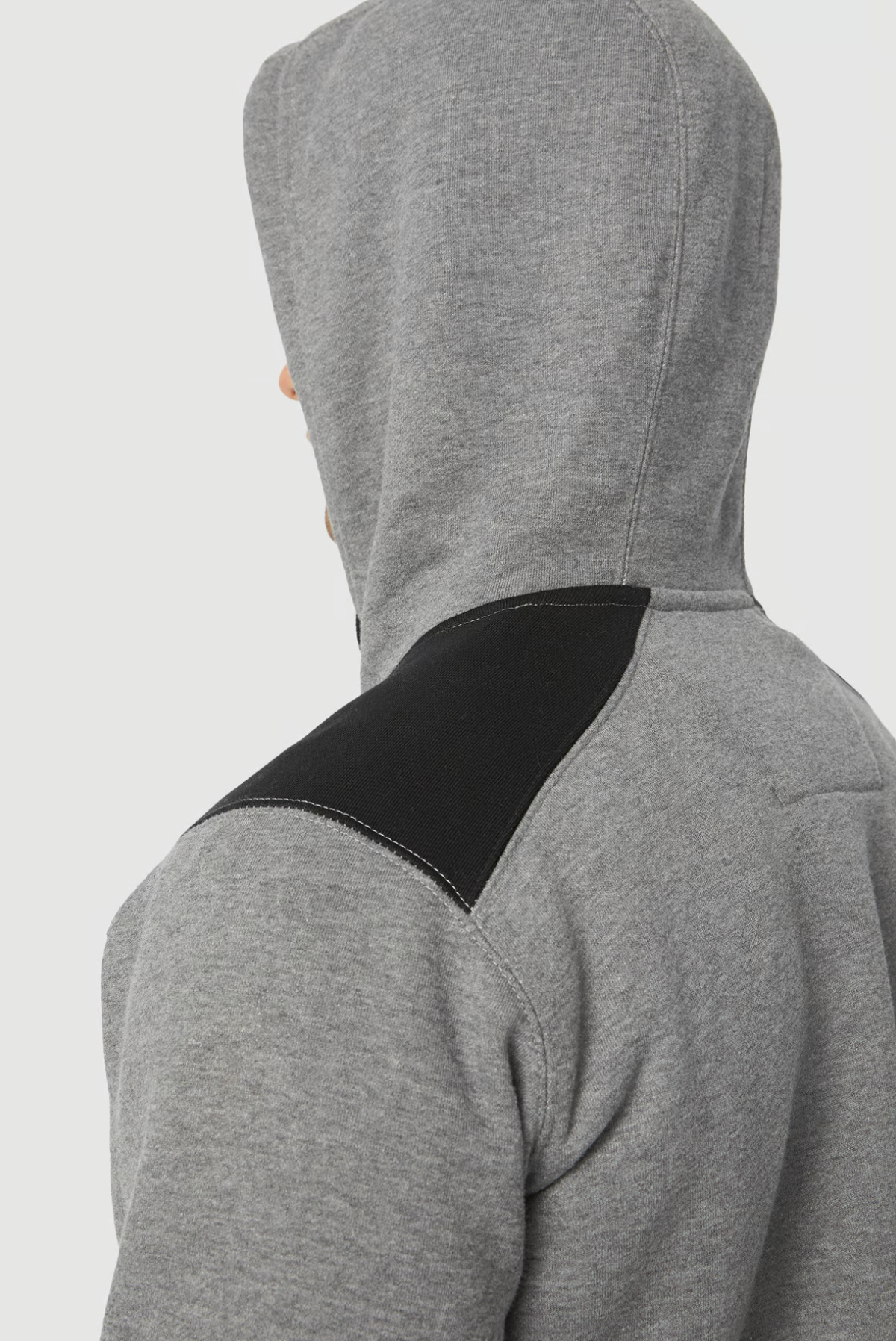 A person is donning a gray CAT Logo Panel Hooded Sweat with a black shoulder patch. The back view emphasizes contrasting shoulder fabric and a hidden velcro phone pocket.