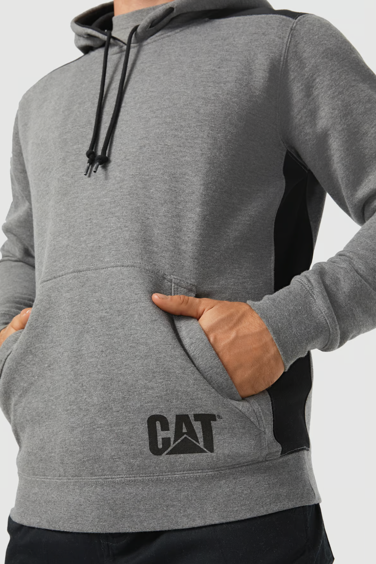 A person wears a gray CAT Logo Panel Hooded Sweat with black drawstrings and side panels, featuring the iconic logo on the front. Their hands are in the hoodie's hidden velcro phone pocket, set against a plain white background.