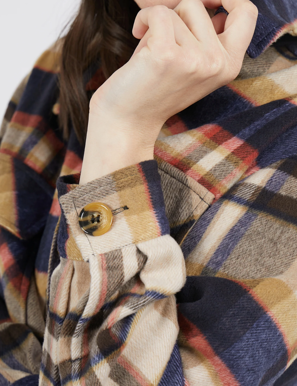 Close-up of a person wearing the Foxwood Noemi Check Shacket in blue, brown, red, and cream plaid. The shacket features buttoned cuffs as the person rests their chin on their hand with fingers partially visible.