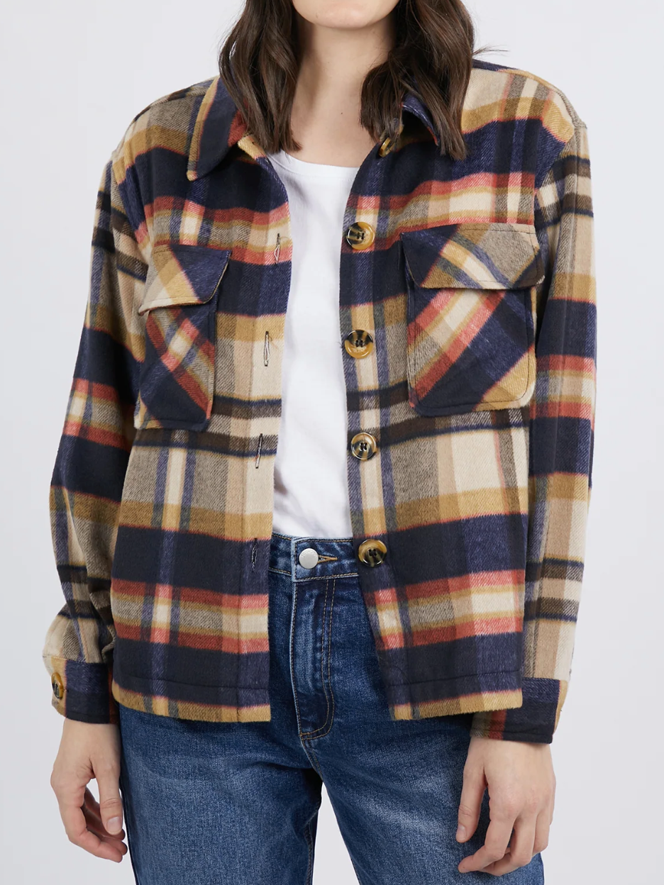 Wearing the Foxwood Noemi Check Shacket in navy, beige, and red plaid over a white t-shirt, paired with blue jeans, they complete the look with dark buttons and buttoned pockets, keeping their face hidden.
