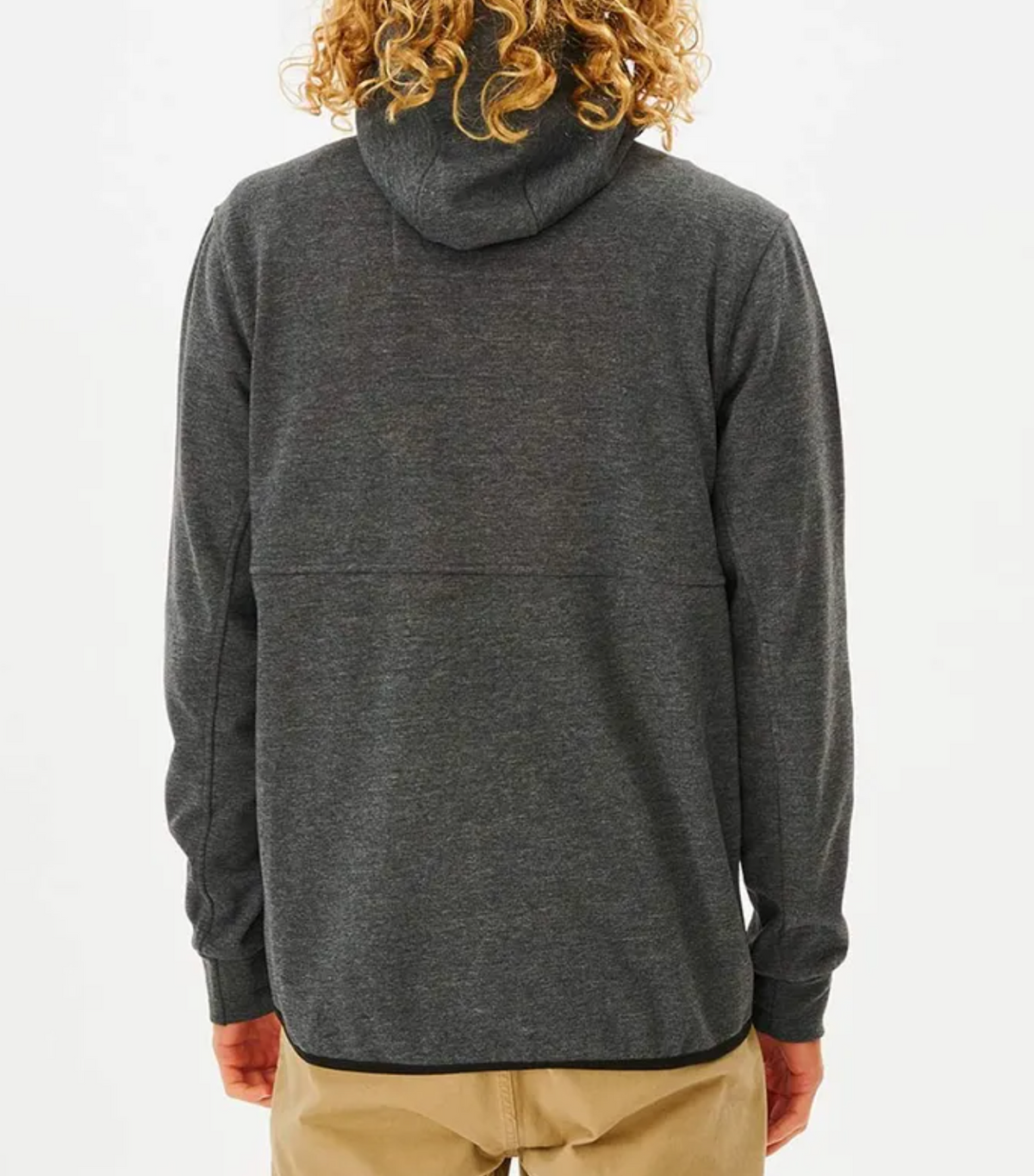 A person with curly hair is seen from behind, wearing a dark gray Rip Curl Anti Series Departed Zip Thru hoodie and tan pants, standing against a white background. It's the perfect winter clothing choice for style and durability.
