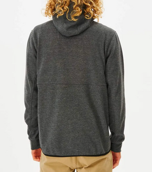 A person with curly hair is seen from behind, wearing a dark gray Rip Curl Anti Series Departed Zip Thru hoodie and tan pants, standing against a white background. It's the perfect winter clothing choice for style and durability.