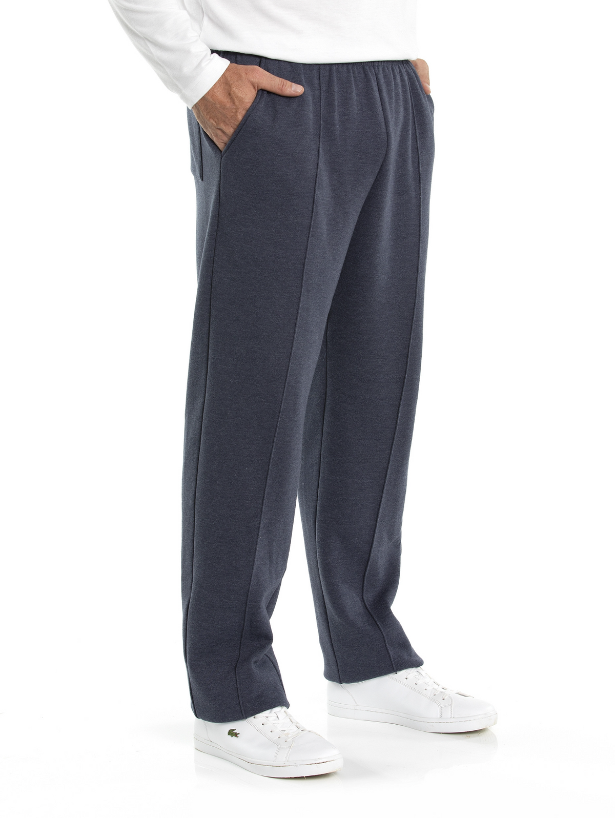A man is wearing a white long-sleeved shirt, Breakaway Snowy Mt Fleece Pants with a seam down the front of each leg, and white sneakers. His hands are in his pockets, and he stands against a white background, perfectly embodying casual weekend wear.