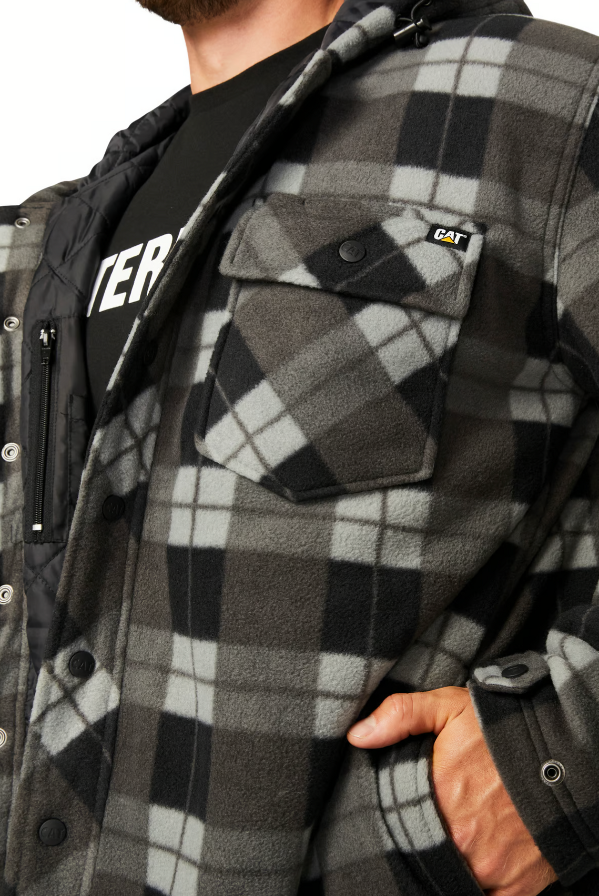 A person wears a CAT Active Work Jacket, an insulated black and gray plaid fleece with a buttoned chest pocket and "CAT" logo patch, over a black T-shirt. One hand is in the jacket pocket; the face is not visible.
