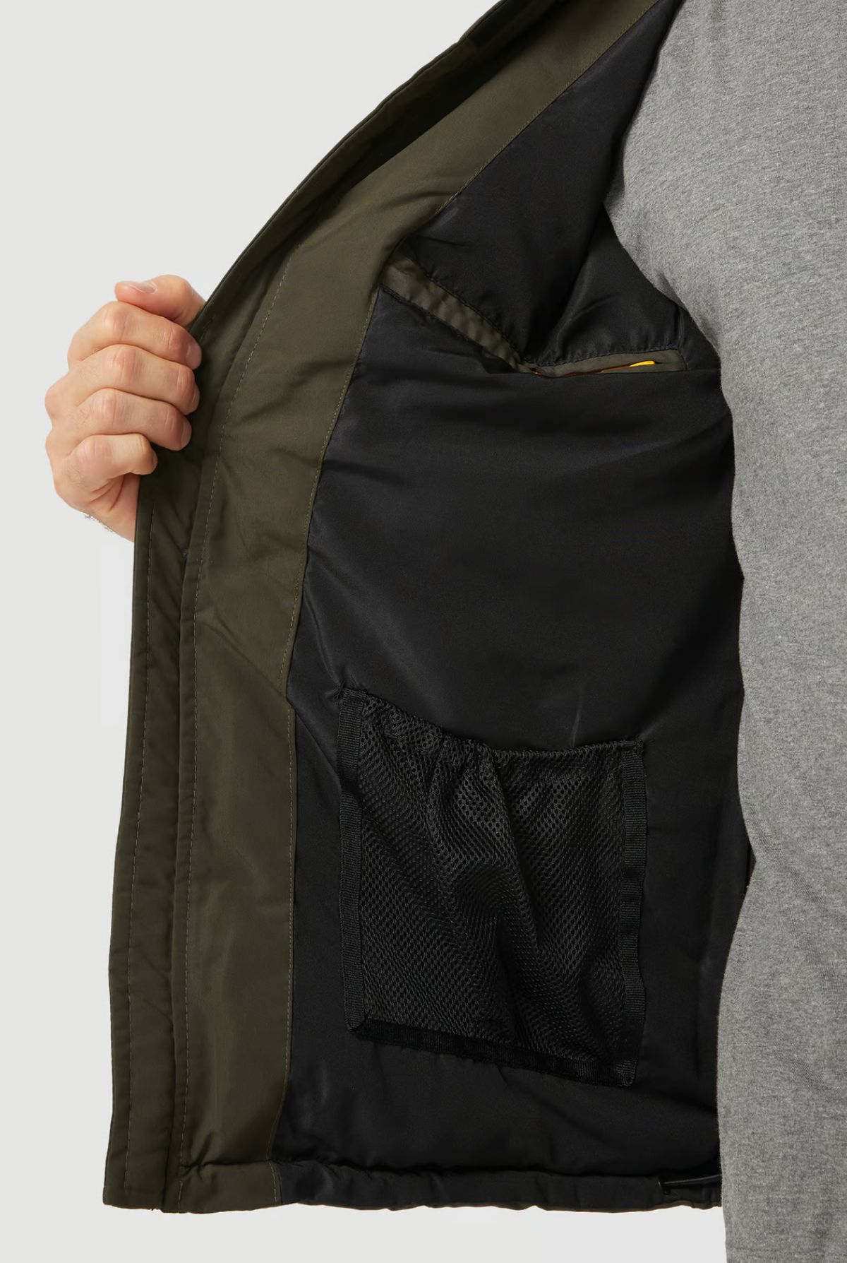 A person in a gray shirt holds open the CAT Arctic Zone Vest, revealing its black inner lining and two inside pockets—one mesh and one zippered. The vest features polyester insulation for warmth.