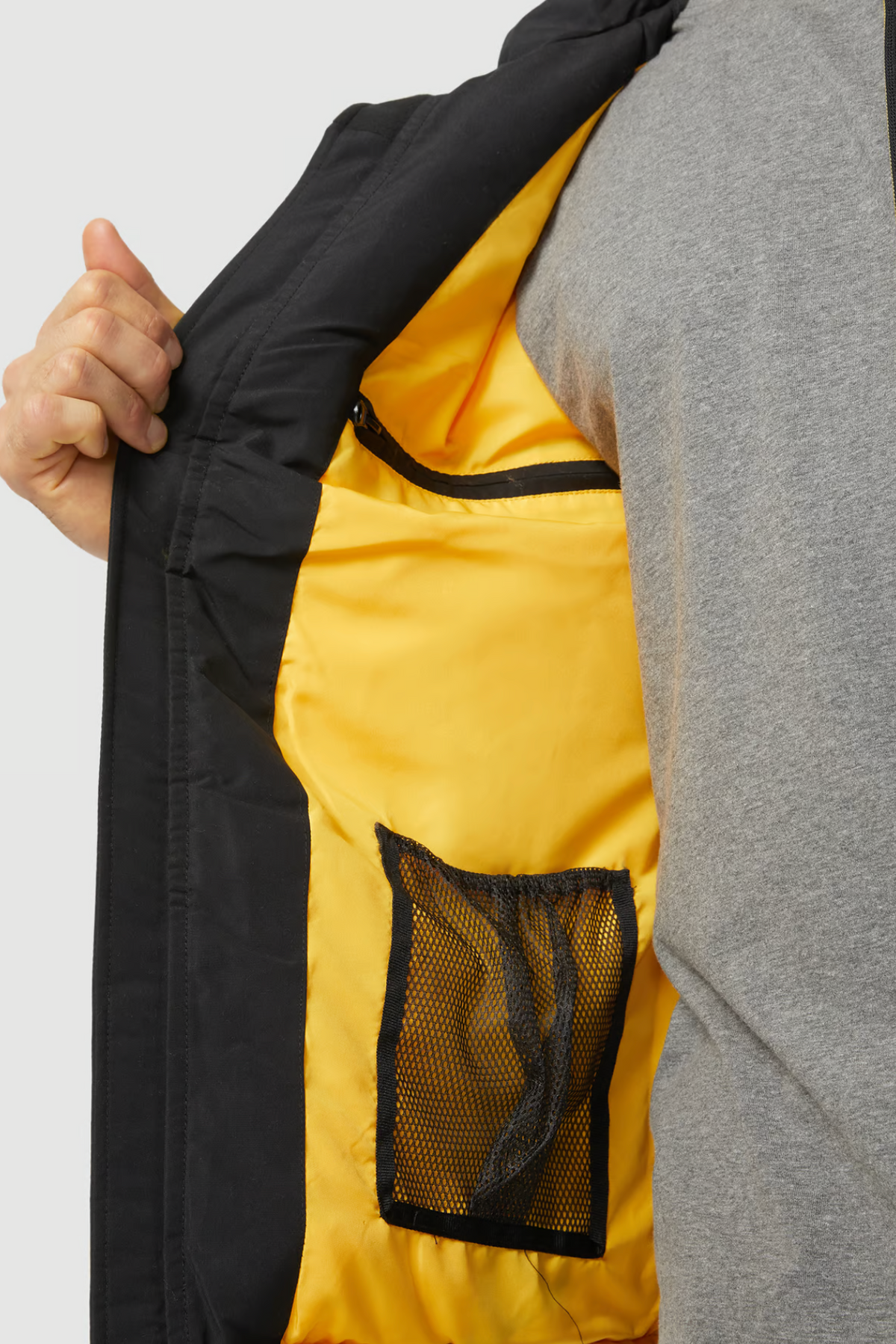 A person in a grey shirt holds open the CAT Arctic Zone Vest, showing its black exterior with an insulated stand-up collar and yellow inner lining featuring a zip pocket and a mesh pocket.