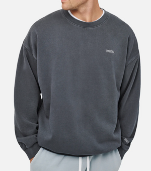 The person sports an oversized dark gray Industrie The Del Sur Sweat, "INDUSTRIE" embroidered on the chest, paired with acid wash light gray pants. Against a plain white background, their face remains hidden.