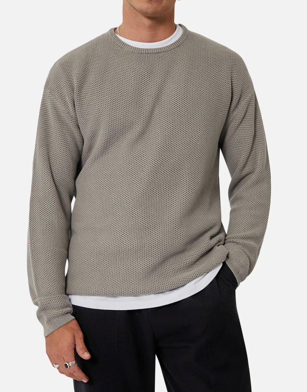 A person is clad in the Industrie The Washed Culver Knit, a comfy gray sweater made of 100% cotton, layered over a white shirt. They pair it with black pants and stand against a plain background, casually tucking their left hand into their pocket.