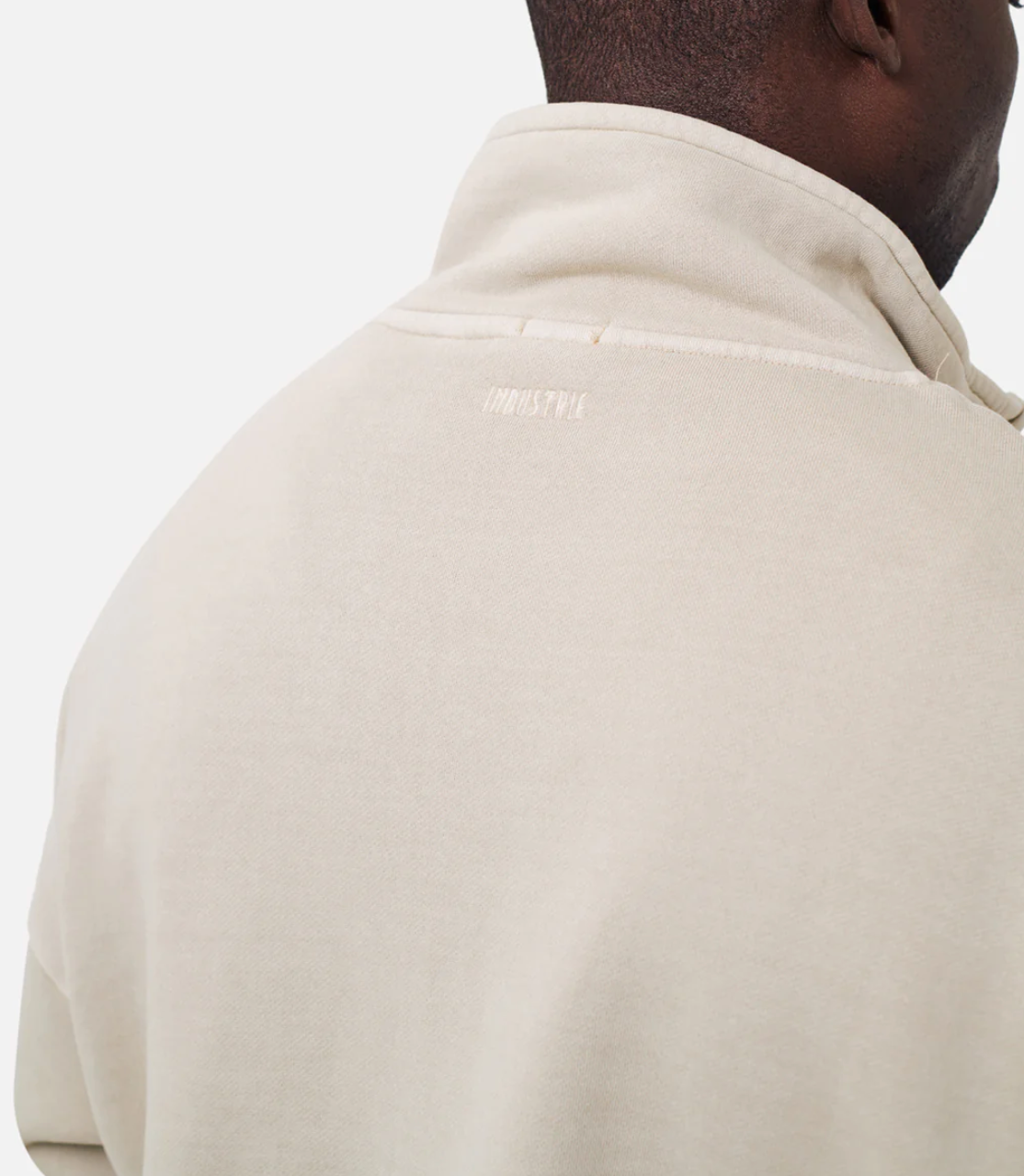 A person is seen from behind wearing a light beige oversized high-neck sweatshirt, labeled as "Industrie The Washed Del Sur Track Top." It features "IMPULSTIV" embroidered just below the collar, highlighting the upper back and neck area.