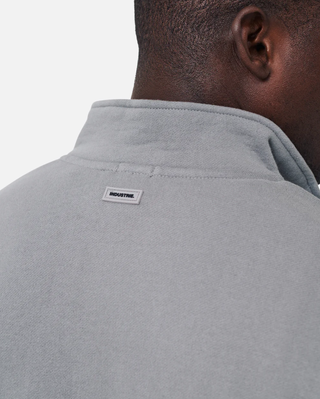 Close-up of a person wearing the Industrie The Del Sur Track Top in gray with an oversized fit. A small rectangular tag reading "INDUSTRIE" is on the back near the neckline, and its soft fleece lining ensures comfortable wear.
