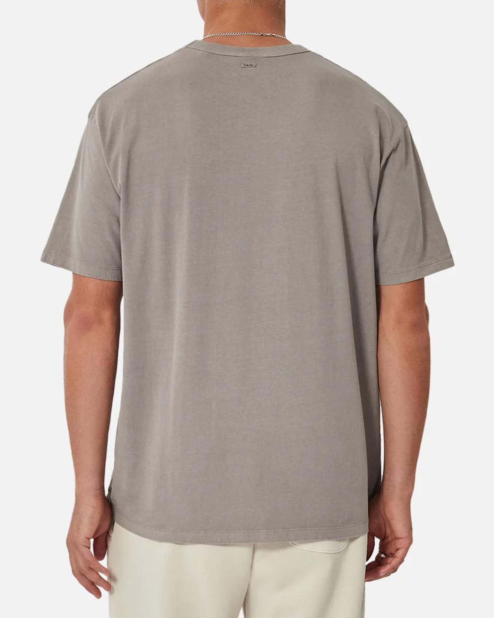 A person is shown from the back wearing an oversized Industrie The Del Sur Tee in plain gray, paired with light-colored pants. Made of 100% cotton, the T-shirt has a small logo below the neckline. They accessorize with a thin chain necklace against a plain white background.