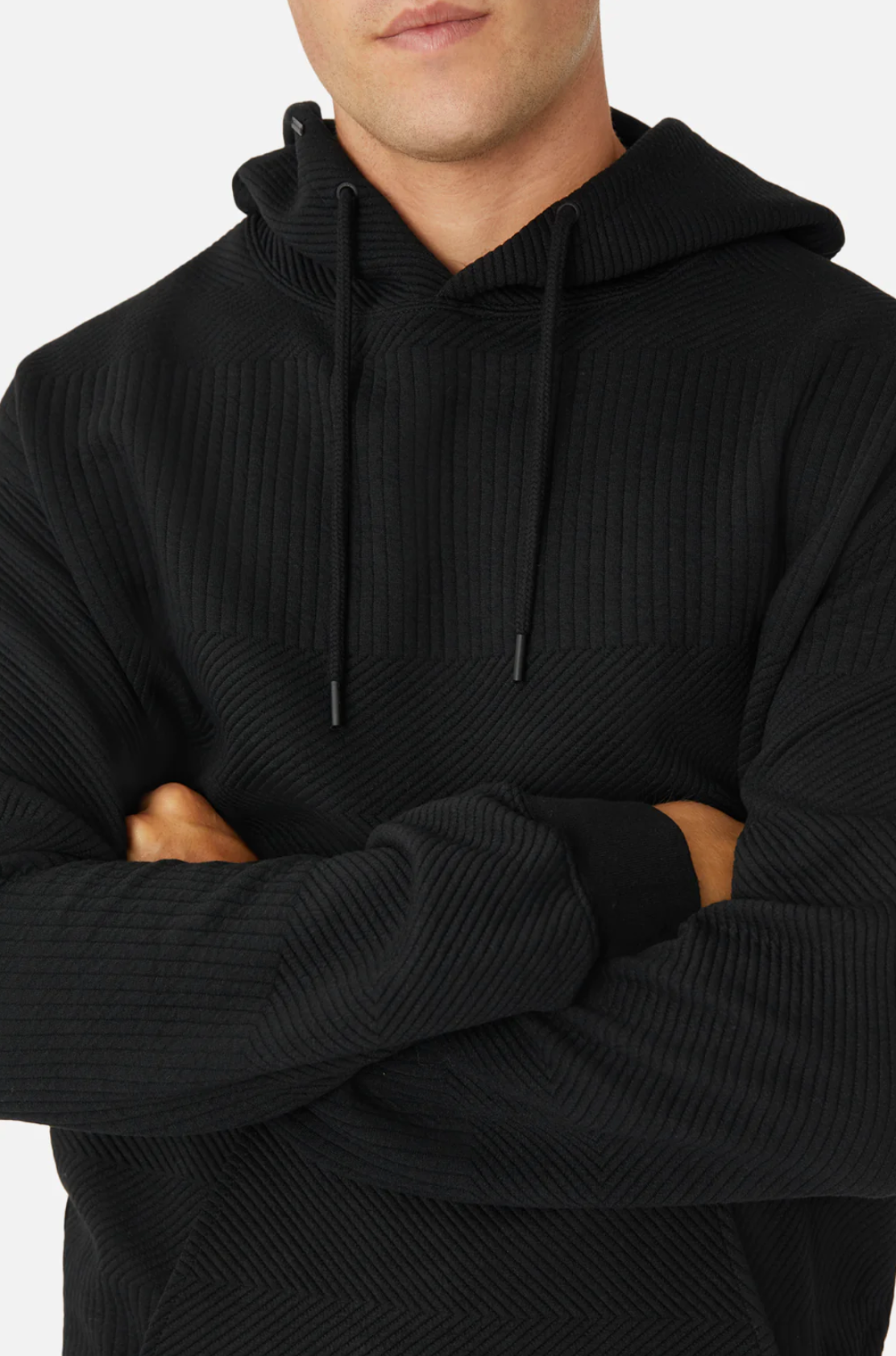 A person in the Industrie The Robinson Hoodie, featuring a textured design, stands with arms crossed against a plain white background. The image showcases the hoodie’s relaxed fit and intricate details, highlighting its elegance.