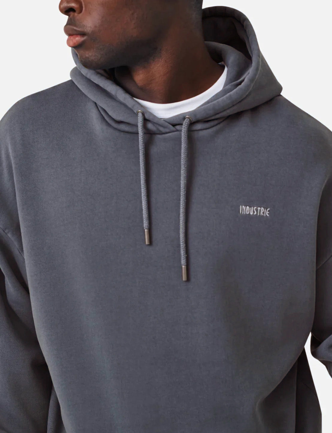 A person wears the Industrie The Del Sur dark gray acid wash hoodie with "INDUSTRIE" on the chest over a white shirt. The comfortable hoodie features drawstrings and an oversized fit as they look to the side against a plain background.