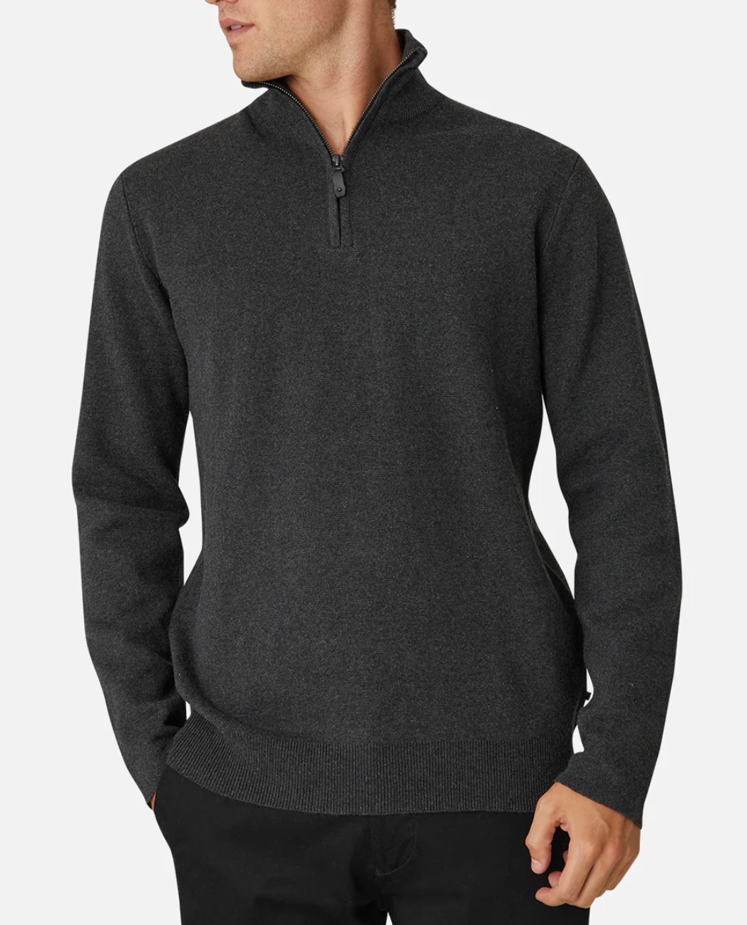 Someone wearing an Industrie The Lakewood Zip Neck, a dark gray sweater with ribbed cuffs and hem, and black pants stands against a white background. Made from 100% cotton, the casual jumper's wearer has their hands in their pockets and is looking to the side.