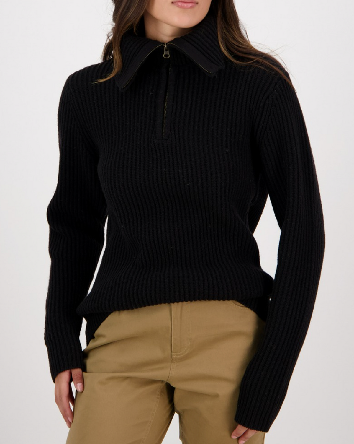 A person wearing the Swanndri Riverside Zip Neck Rib Jumper, a black lambswool sweater with a zip-up collar, pairs it with khaki pants against a plain white background.