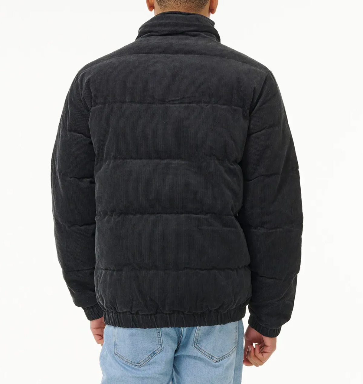 A person wearing a black Rip Curl Rincon Cord Puffer Jacket with padded lining and light blue jeans stands facing away, displaying the back of the jacket against a plain white background.