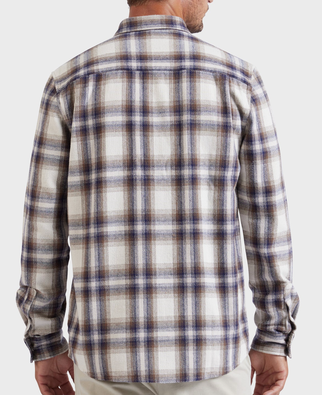 A person is shown from the back, wearing the Academy Brand Colorado Shirt—a long-sleeve, button-up shirt with a white, blue, and brown plaid pattern. This stylish shirt is crafted from 100% cotton and features a collar. The person’s hands are not visible as their arms hang relaxed at their sides. The background is plain white.