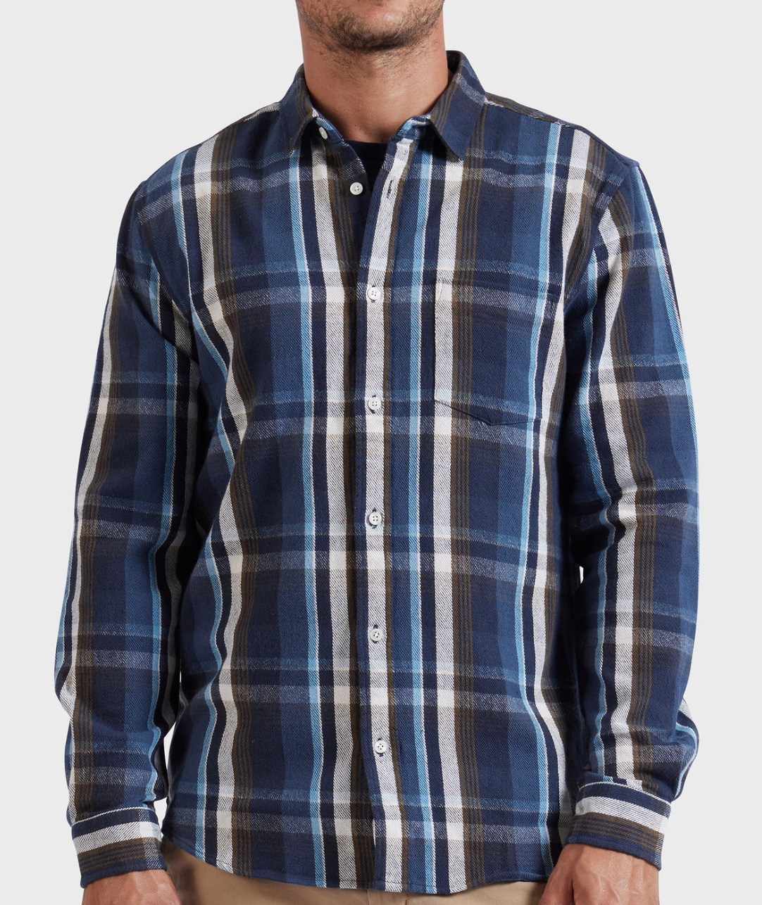A man wears the Academy Brand So Cal Shirt, a 100% cotton plaid long-sleeve button-up in blue, white, and brown, while standing against a plain light gray background. His face is partially out of frame.